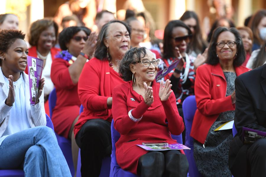 a group of women wearing red sweaters clap for the performers standing ahead out of focus